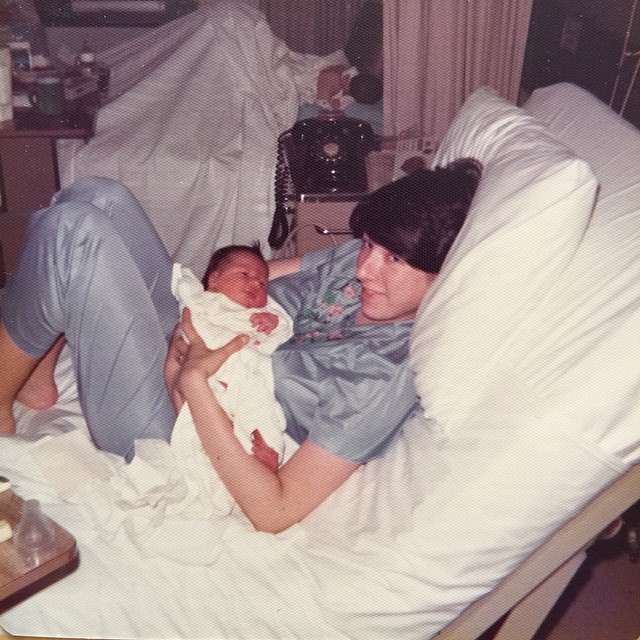 My mother and me on my birthday. Note the shared postpartum room with only a curtain separating the mothers from one another.
